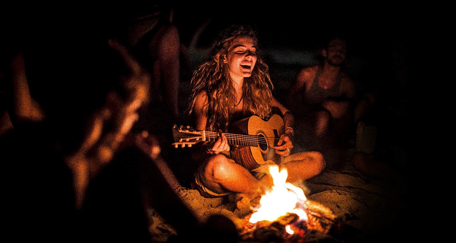 Guirl playing guitar on the beach with friends by the fire
